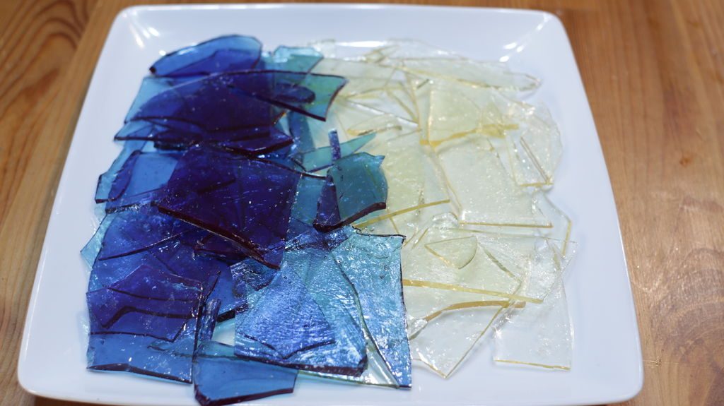 Blue and clear edible sugar glass on a white plate on a wooden table